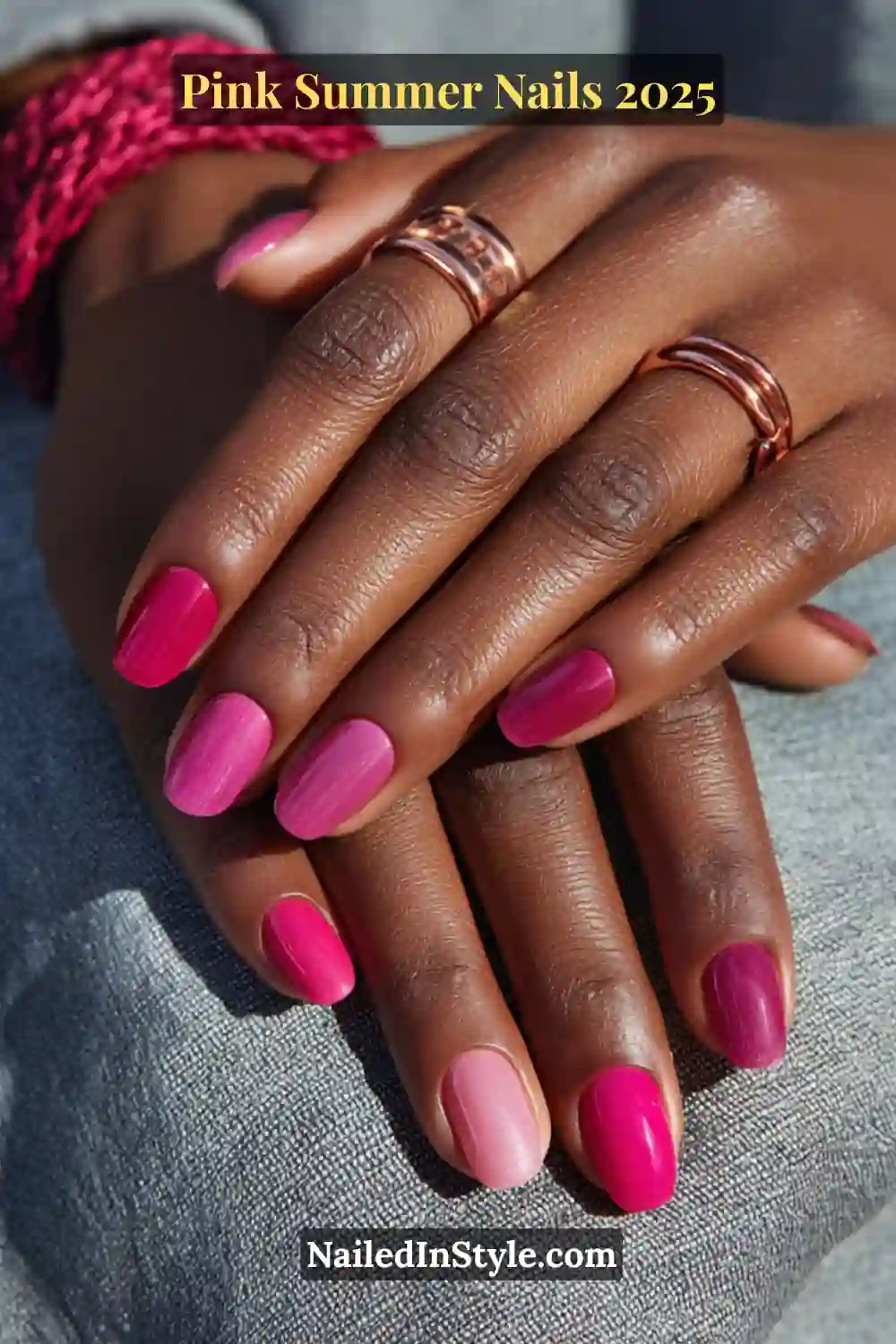 Close-up of deep skin hand with short round nails in hot pink, magenta, and berry pink glossy polish