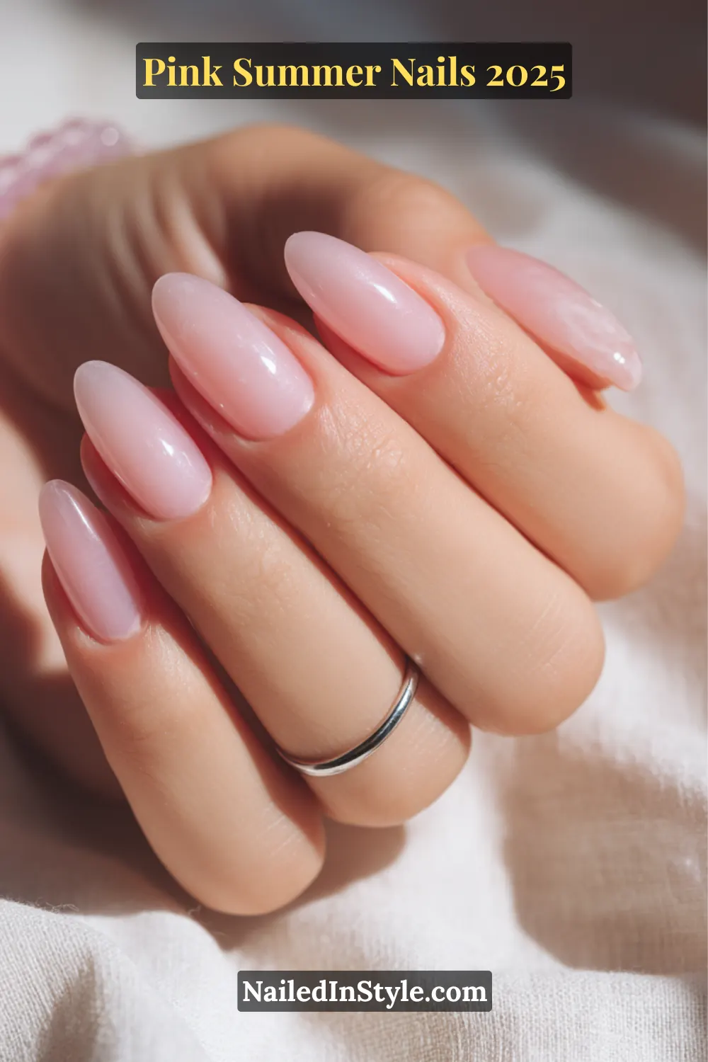 Close-up of almond-shaped nails in sheer baby pink polish on fair skin with silver ring