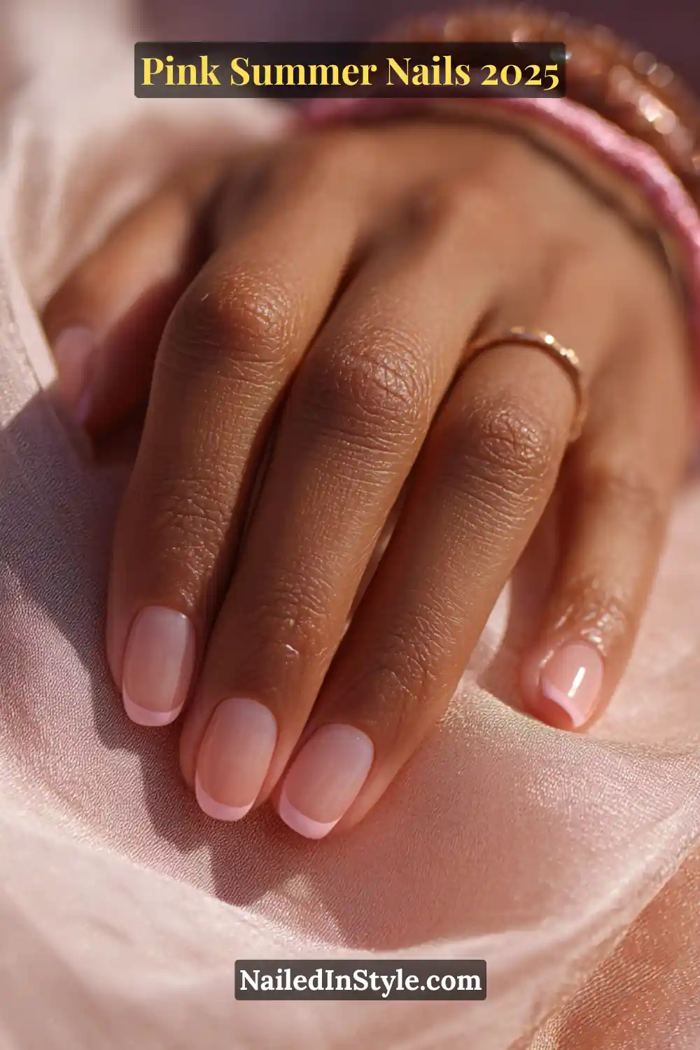 Close-up of a hand with light pink French tips on natural round nails, styled with gold ring and pink bracelets