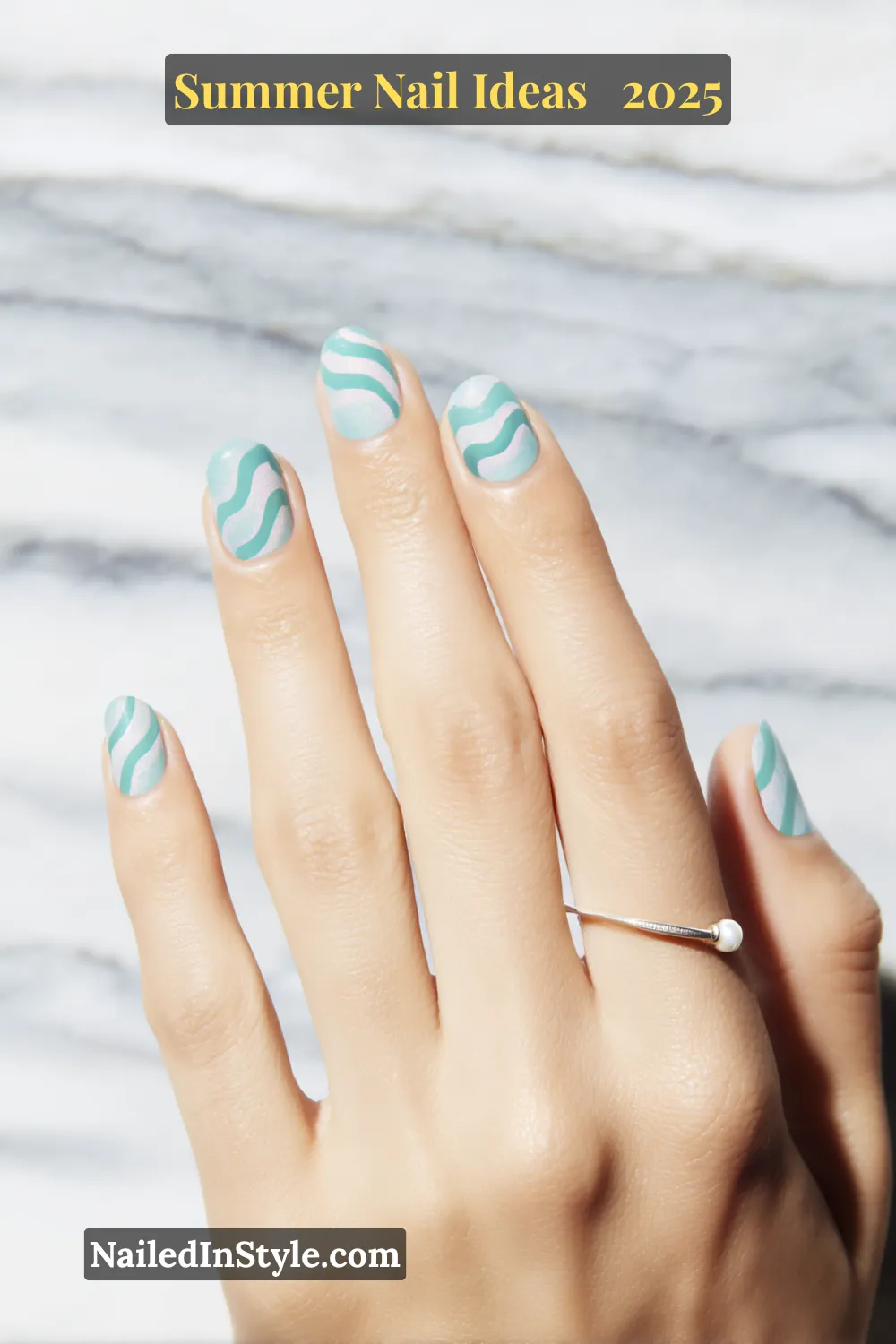 Close-up of hand with short round nails painted in wavy teal ripple patterns over a soft blue base, finished with a pearlized shimmer.