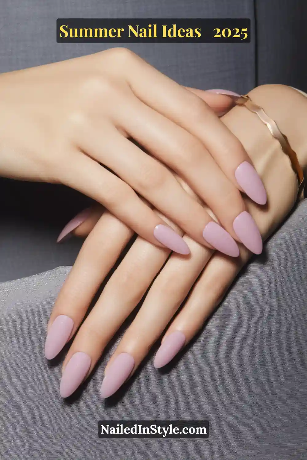 Close-up of porcelain-toned hands with almond-shaped nails painted in a glossy grape jelly hue, topped with a fine shimmer overlay, resting on soft grey fabric with a gold wave bracelet.