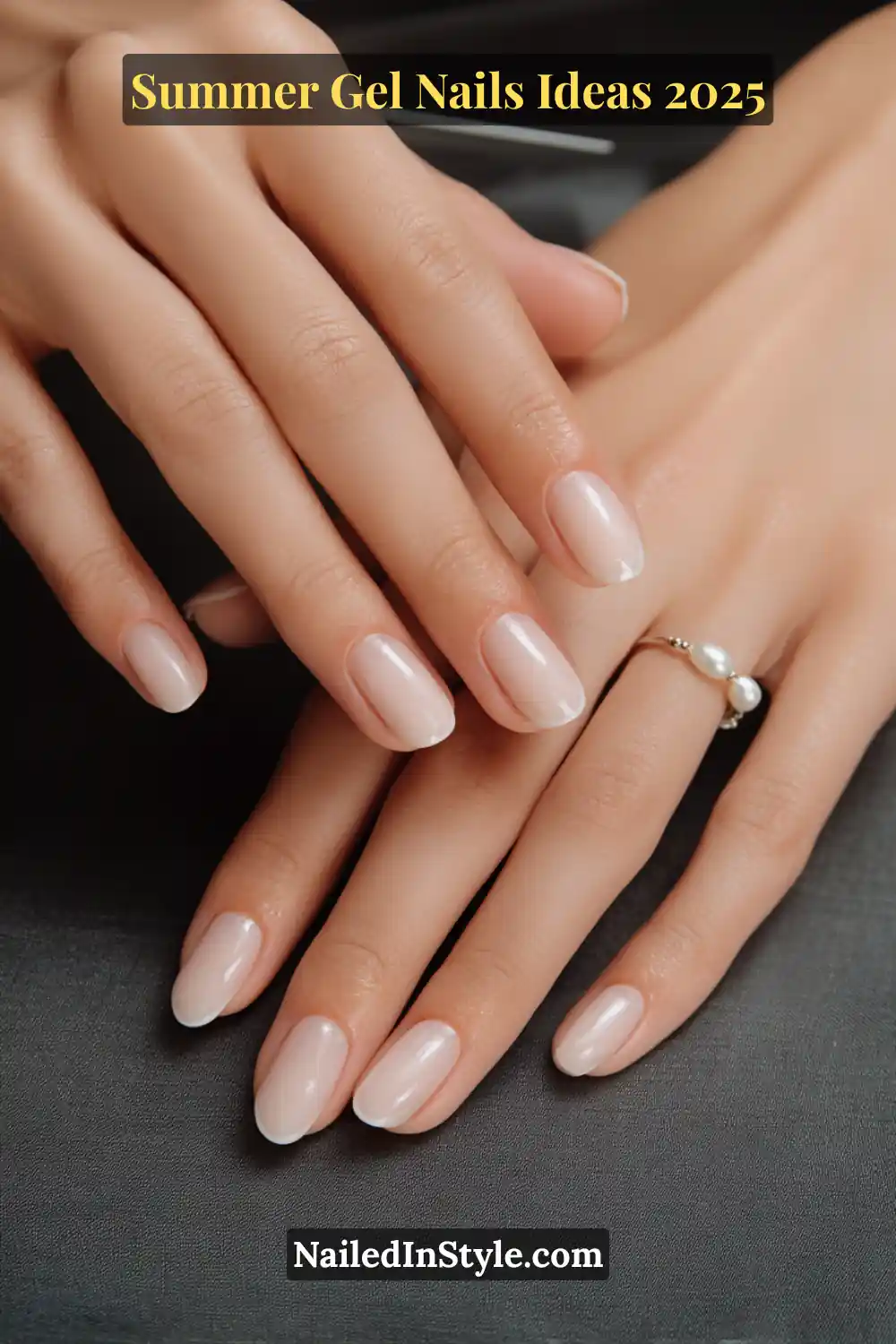Summer Gel Nails Ideas 2026 5 Close-up of porcelain-toned hands with short, rounded gel nails in a sheer nude base and soft milky white French tips, photographed against dark satin fabric with a delicate pearl ring.
