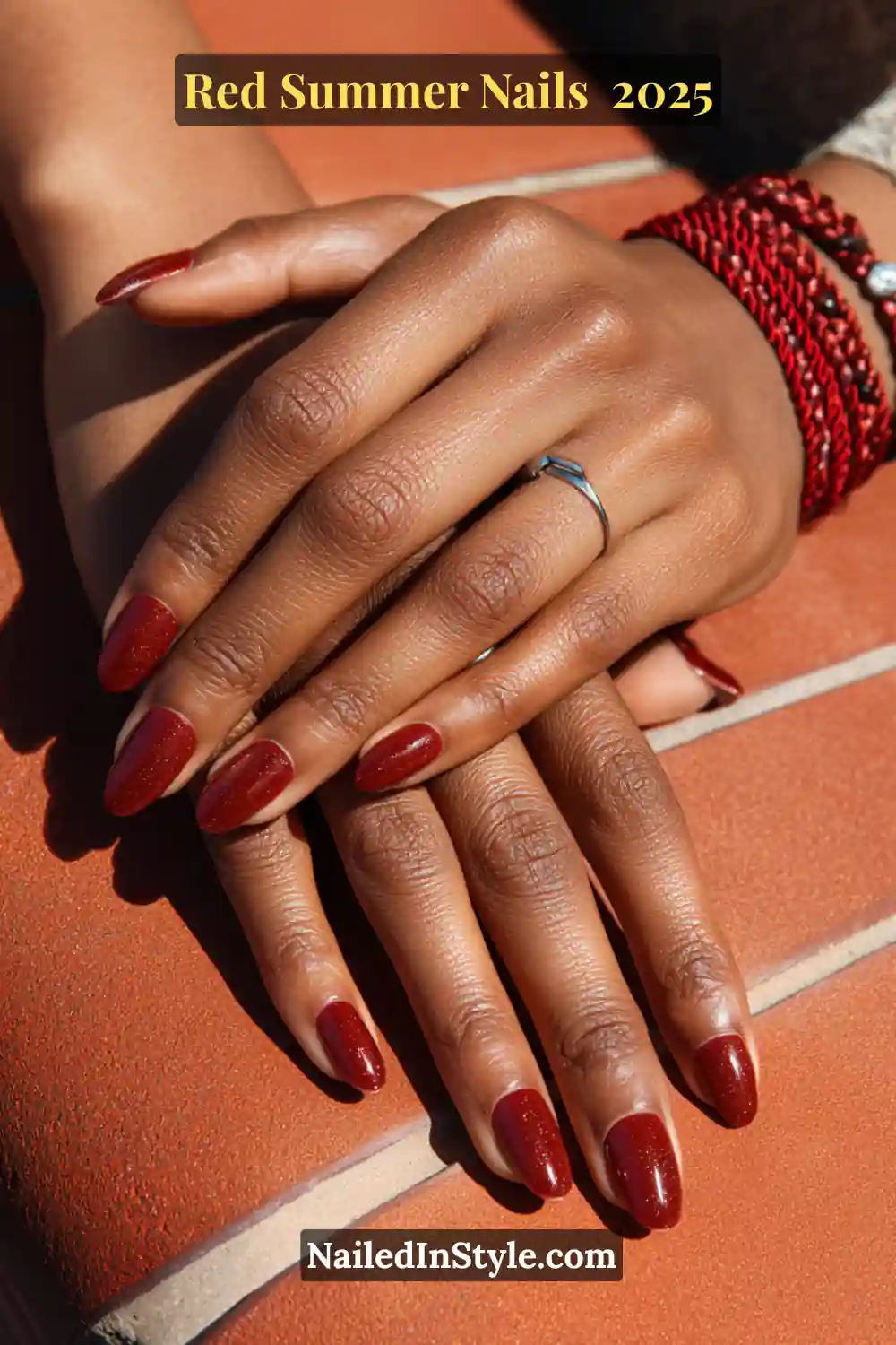Red Summer Nails 2026: Bold, Fiery & Classic Warm-Weather Looks 8 Dark-skinned hands with glossy red BIAB almond nails, resting on terracotta tiles with red bracelets