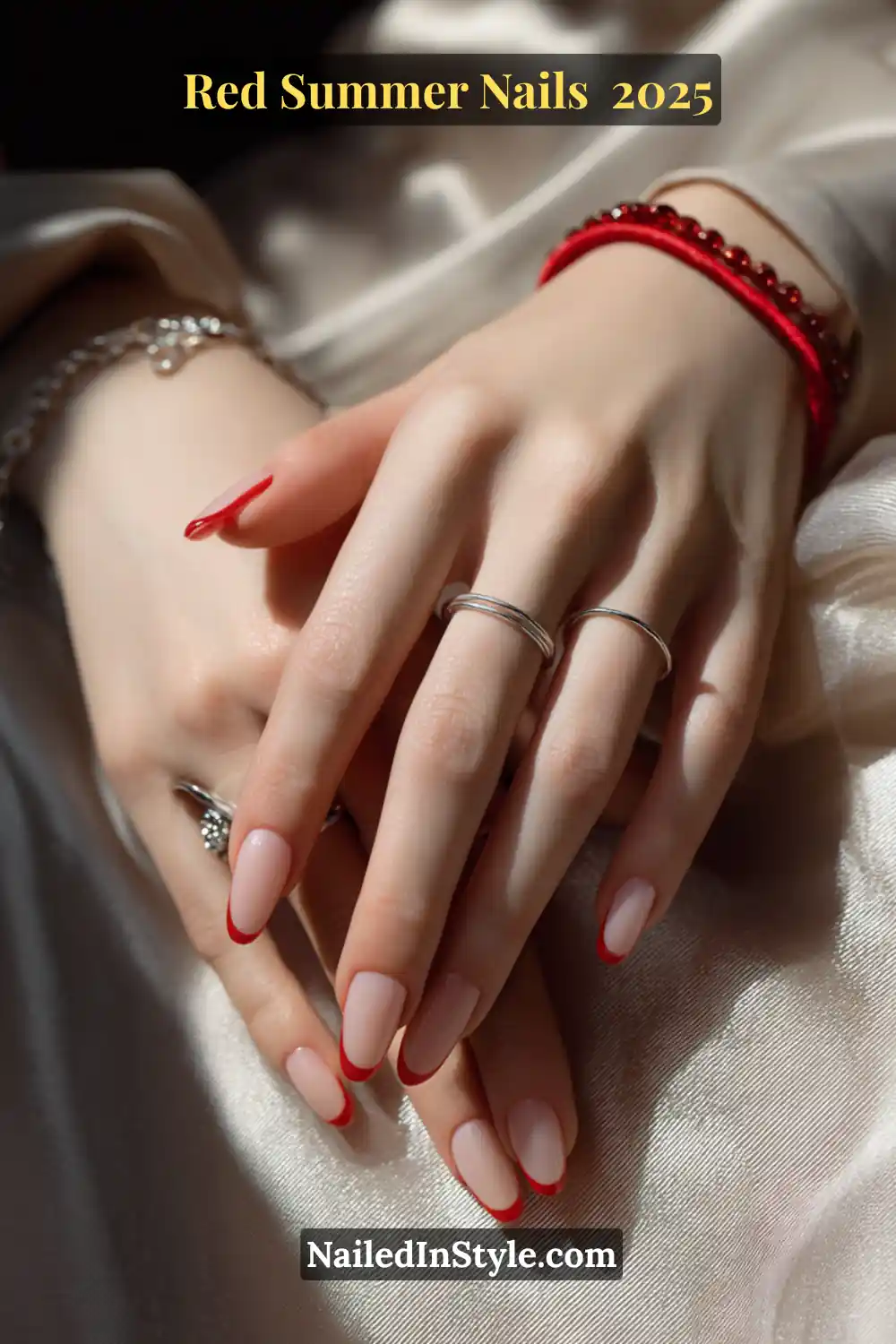 Red Summer Nails 2026: Bold, Fiery & Classic Warm-Weather Looks 10 Elegant hands with red French tip nails on a nude base, wearing silver rings and resting on satin fabric