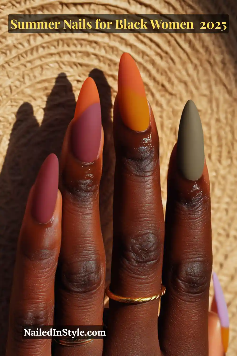 Close-up of a Black woman’s hand with long almond nails in matte orange, brick red, goldenrod, and deep sage green polish, accented by sunlight and gold rings.
