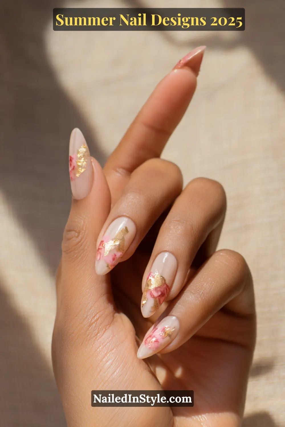Hand with almond-shaped nails featuring blush pink floral art and gold foil on a nude base