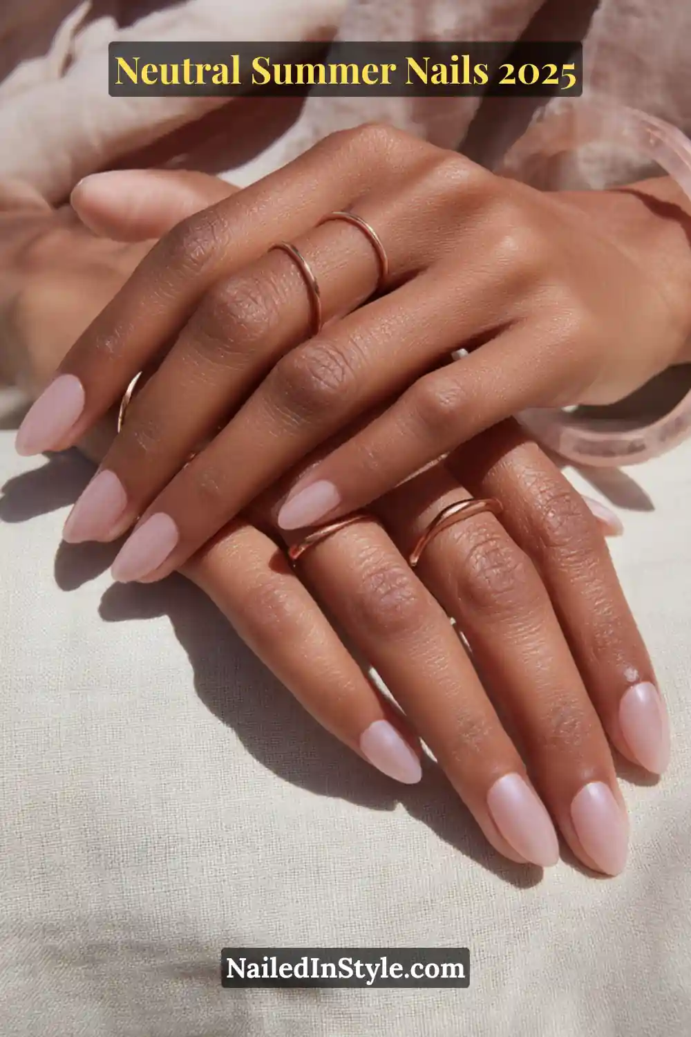 Neutral Summer Nails 2026: Clean, Chic & Warm-Weather Ready 10 Elegant hands with almond-shaped nails in a soft rose-toned polish and high-gloss topcoat, styled with delicate rose-gold rings against a sunlit background.