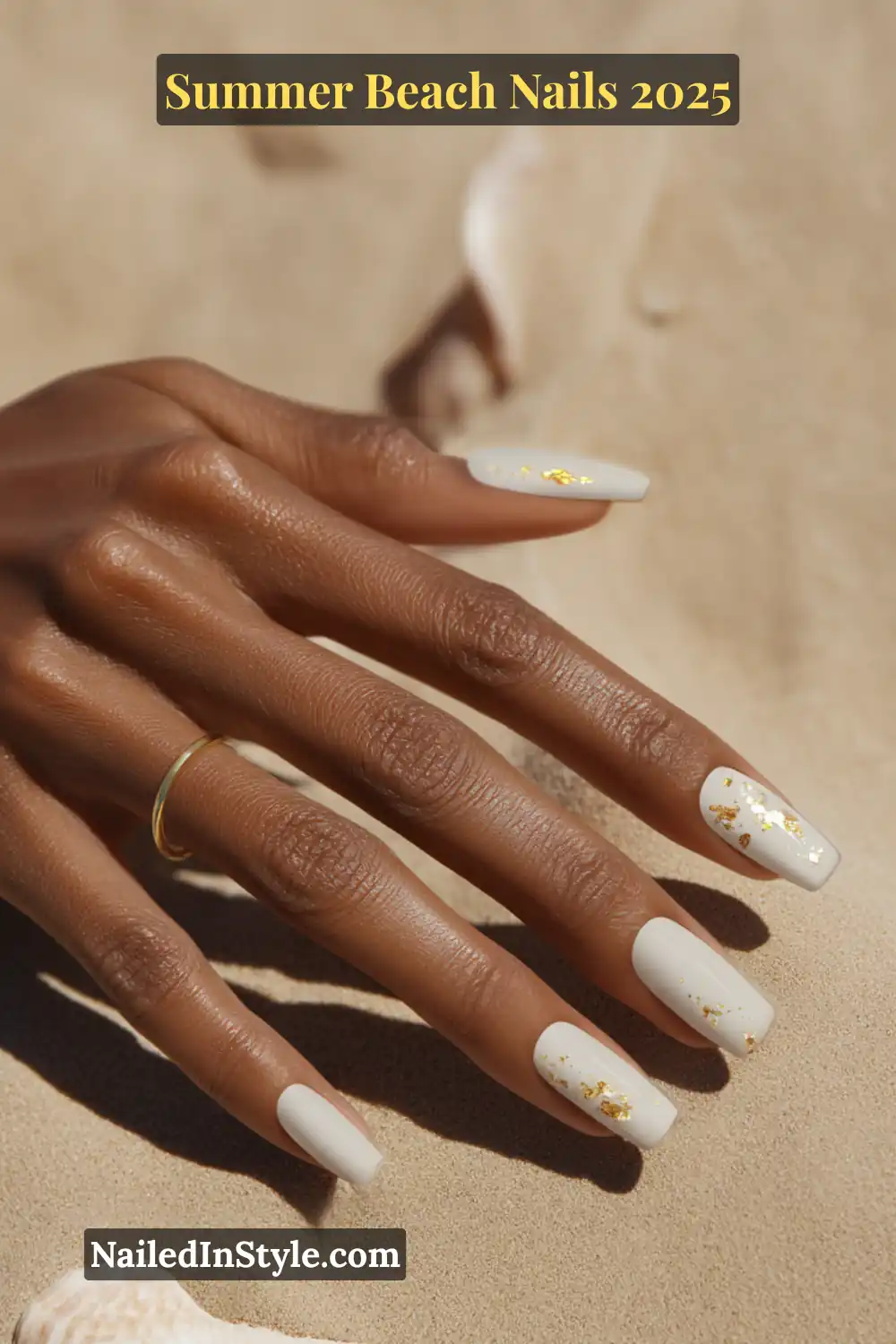 Summer Beach Nails 2026: Tropical, Trendy & Totally You 5 Close-up of a woman’s hand with long square white nails featuring subtle gold foil flakes, posed on sandy beach