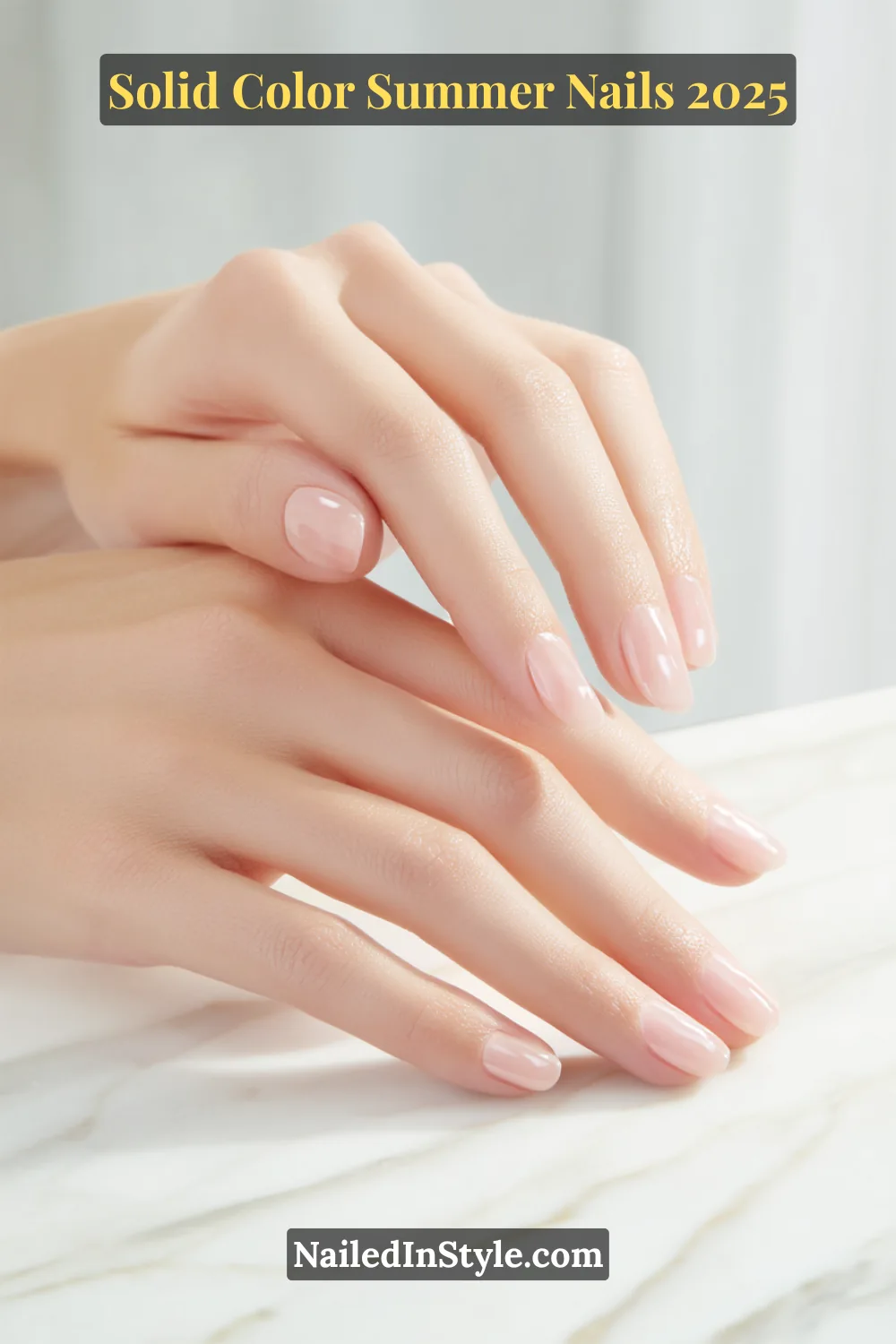 Two hands with short natural-shaped nails painted in a glossy sheer pink polish, resting on a marble surface.
