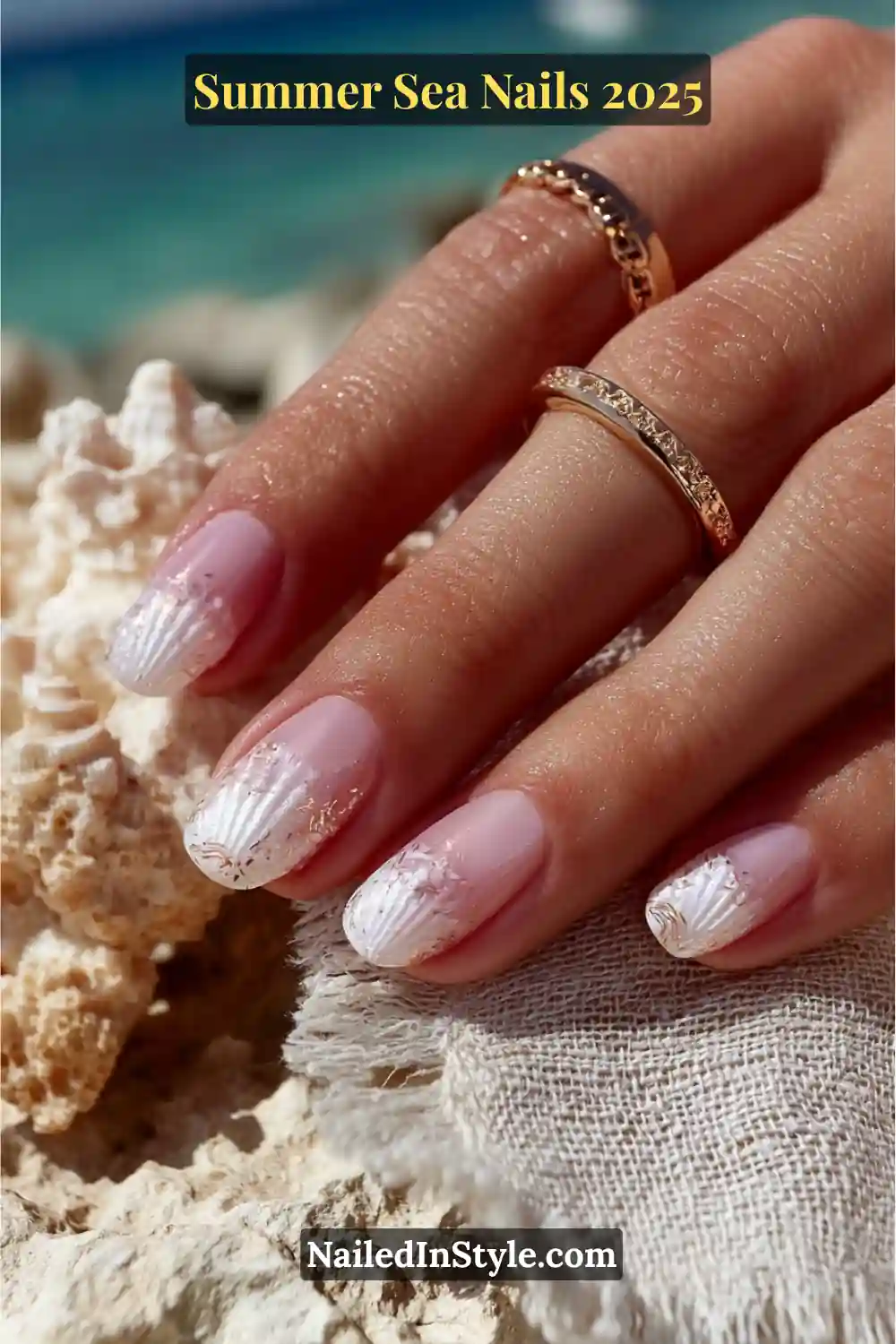 Close-up of hand with pink nude nails featuring white seashell texture stamping and gold foil details