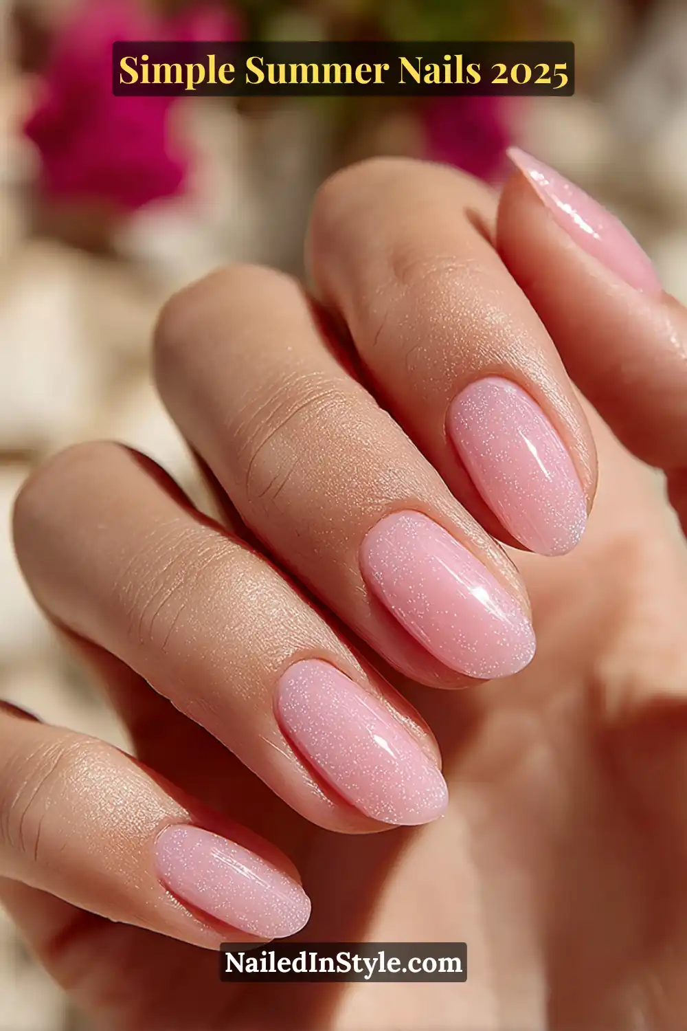 A soft natural hand with medium skin tone features short almond nails painted in a translucent baby pink base with fine shimmer, photographed under bright sunlight with blurred summer florals in the background.