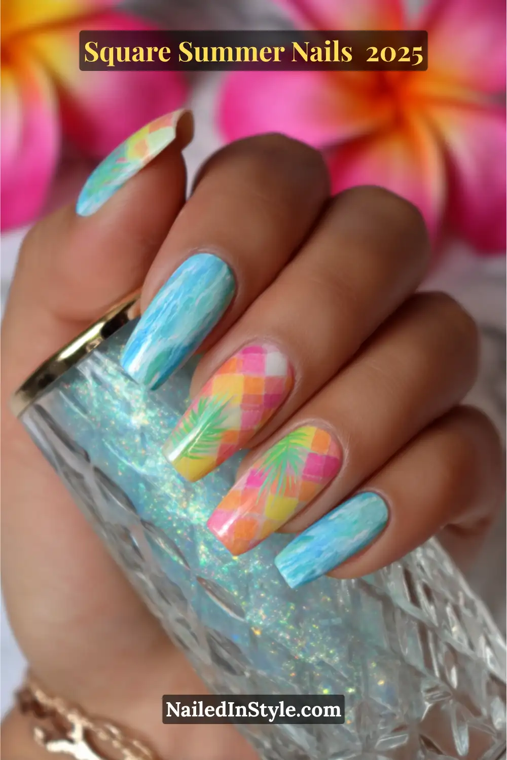 Colorful square nails with rainbow checkerboard and palm leaf art, held against a glittery glass and bright tropical flower background