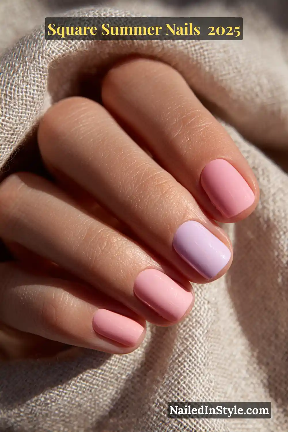 Natural hand with short square nails painted in soft pastel pink and lavender shades, resting on textured beige fabric in sunlight
