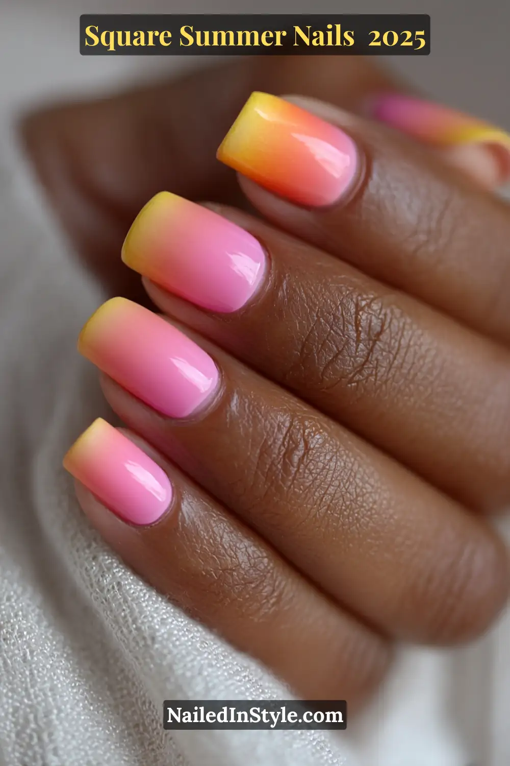 Close-up of a dark-toned hand with square-shaped ombré nails in a smooth sunset gradient of yellow, orange, and pink