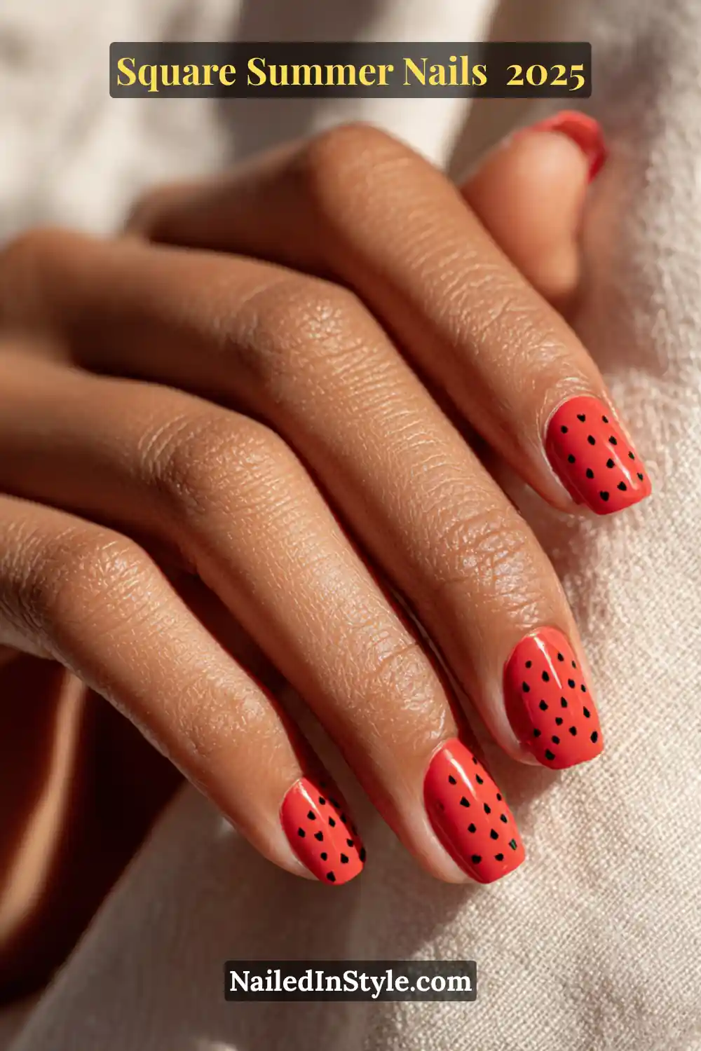 Close-up of a medium-deep toned hand with square red nails featuring playful black dot patterns, resembling watermelon seeds