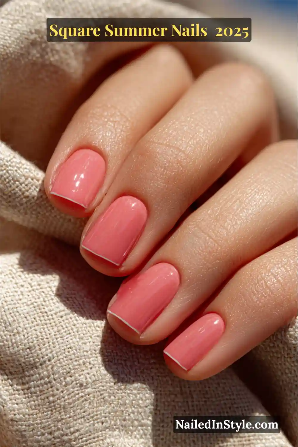 Square Summer Nails Natural hand with light skin tone featuring short square-shaped nails painted in glossy coral pink, resting against a woven summer fabric