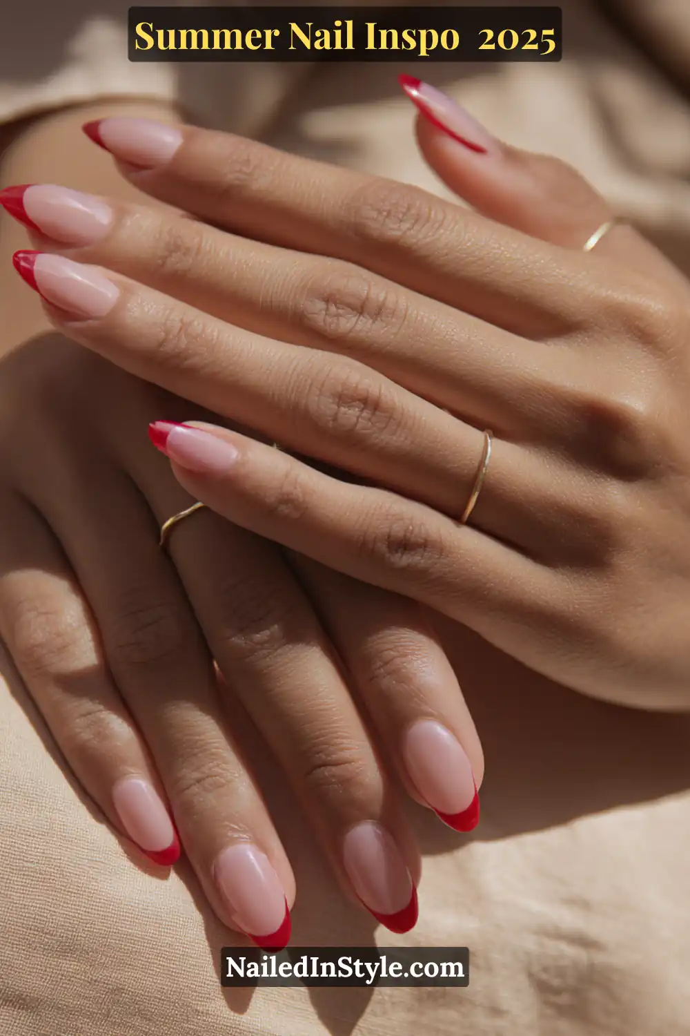 Close-up of hands with almond-shaped nails featuring a sheer blush pink base and glossy red French tips in a strawberry-inspired design.