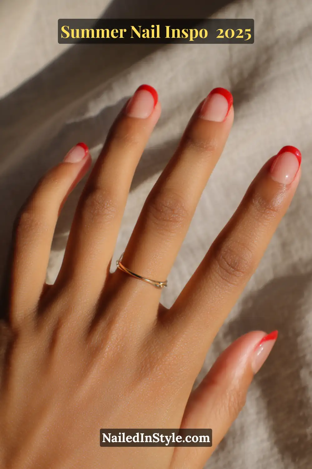 Close-up of a hand with short natural-shaped nails featuring a sheer blush pink base and glossy strawberry red French tips.