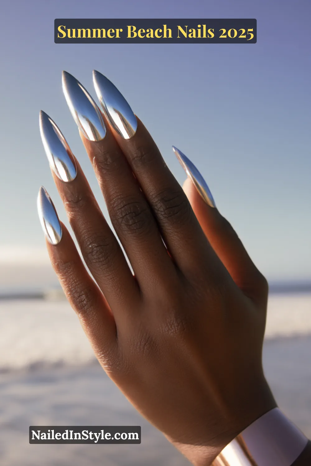 Summer Beach Nails 2026: Tropical, Trendy & Totally You 13 Hand with long stiletto-shaped chrome blue nails reflecting sky, worn on deep skin tone