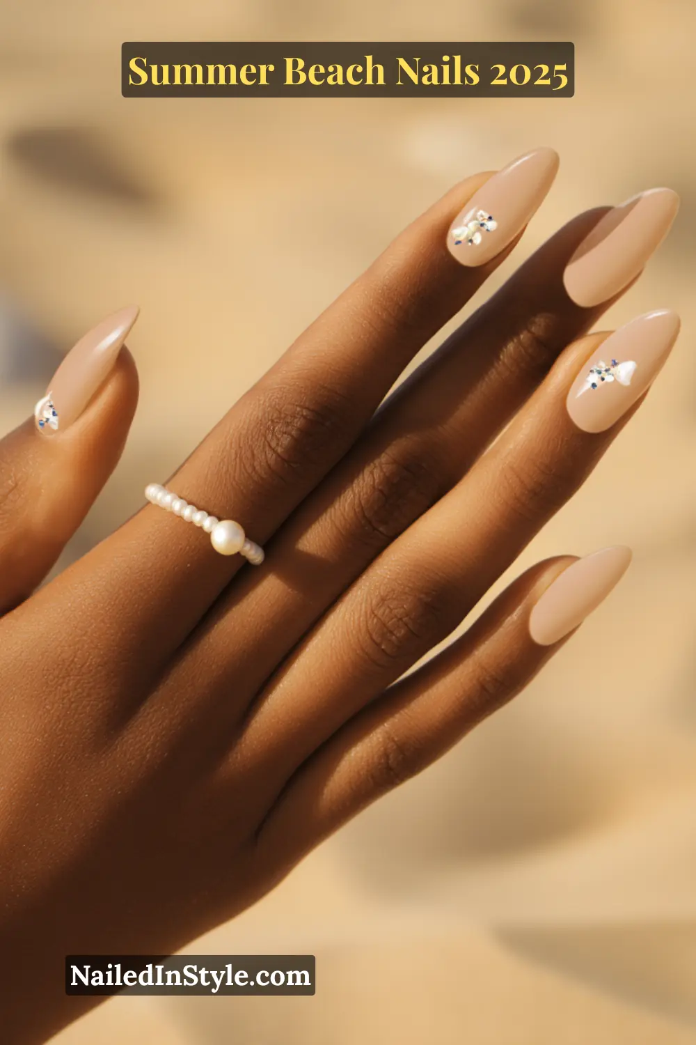 Summer Beach Nails 2026: Tropical, Trendy & Totally You 17 Close-up of nude almond nails with delicate seashell and rhinestone studs on a woman’s hand with pearl ring