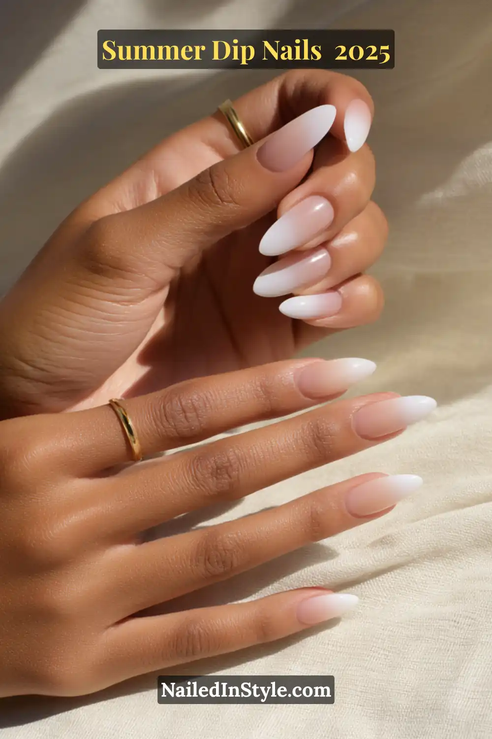 Elegant almond-shaped nails with a white-to-nude gradient fade, shown on softly lit hands with gold rings.