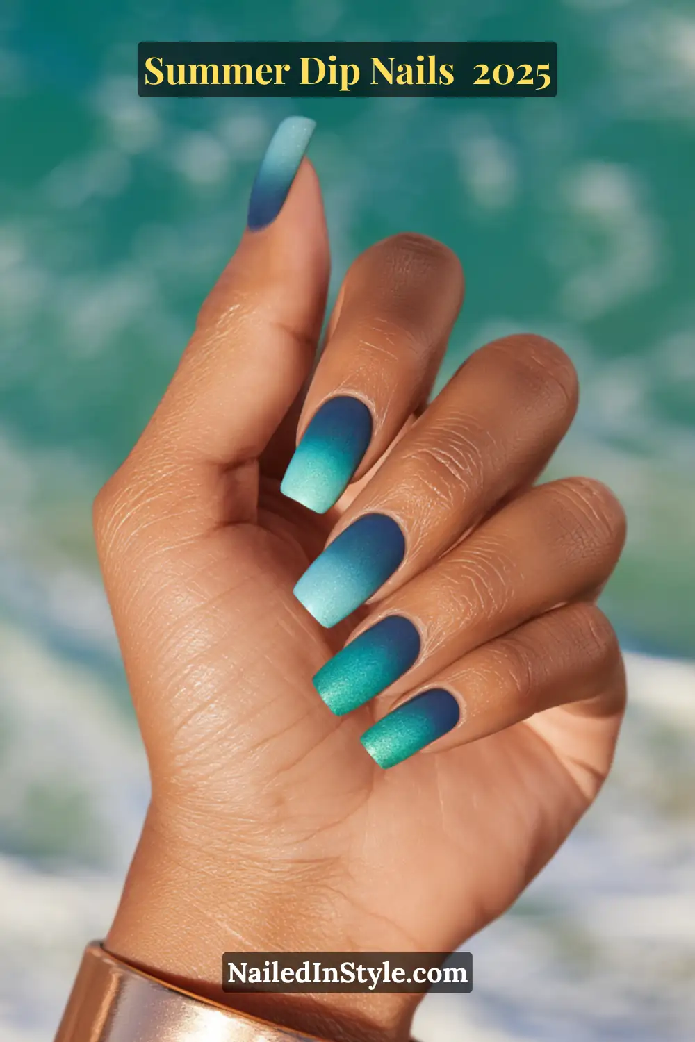 Close-up of a hand with medium-length square nails featuring a deep blue to teal gradient, ocean waves blurred in the background.