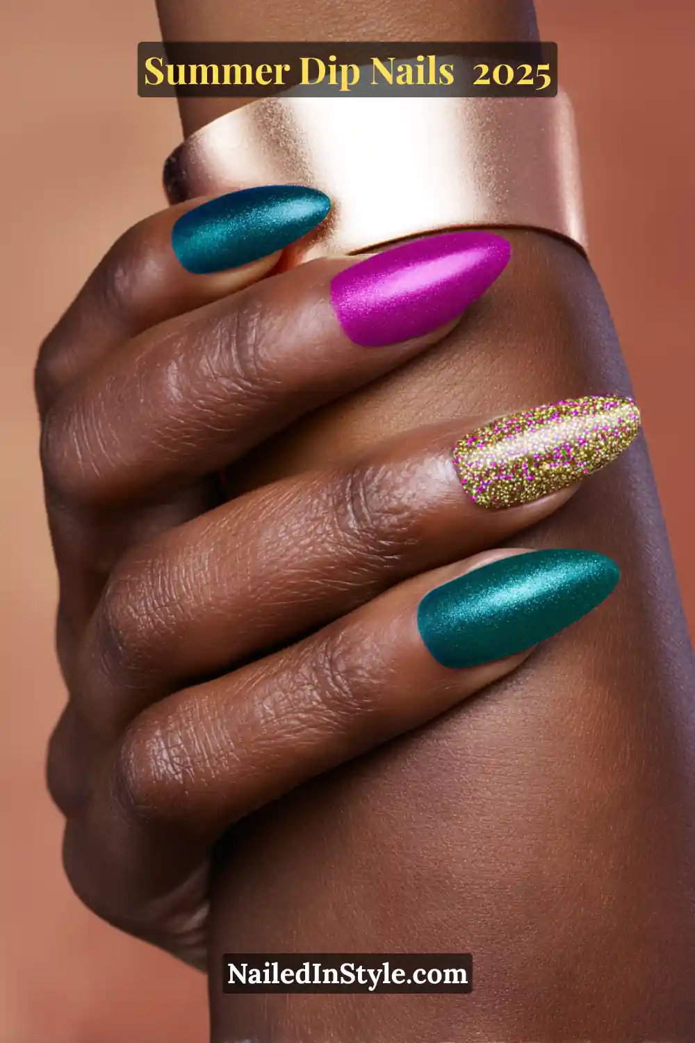 Close-up of a hand with almond-shaped dip nails in deep teal, fuchsia pink, and glittering gold over rich skin.