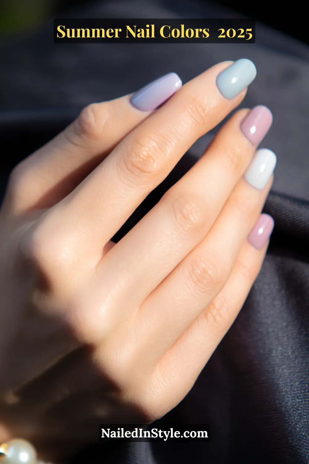 Hottest Summer Nail Colors 2026: Bold, Breezy & On-Trend 7 Close-up of fair-skinned hand with soft pink, baby blue, and lilac nail polish against a silky dark fabric background.