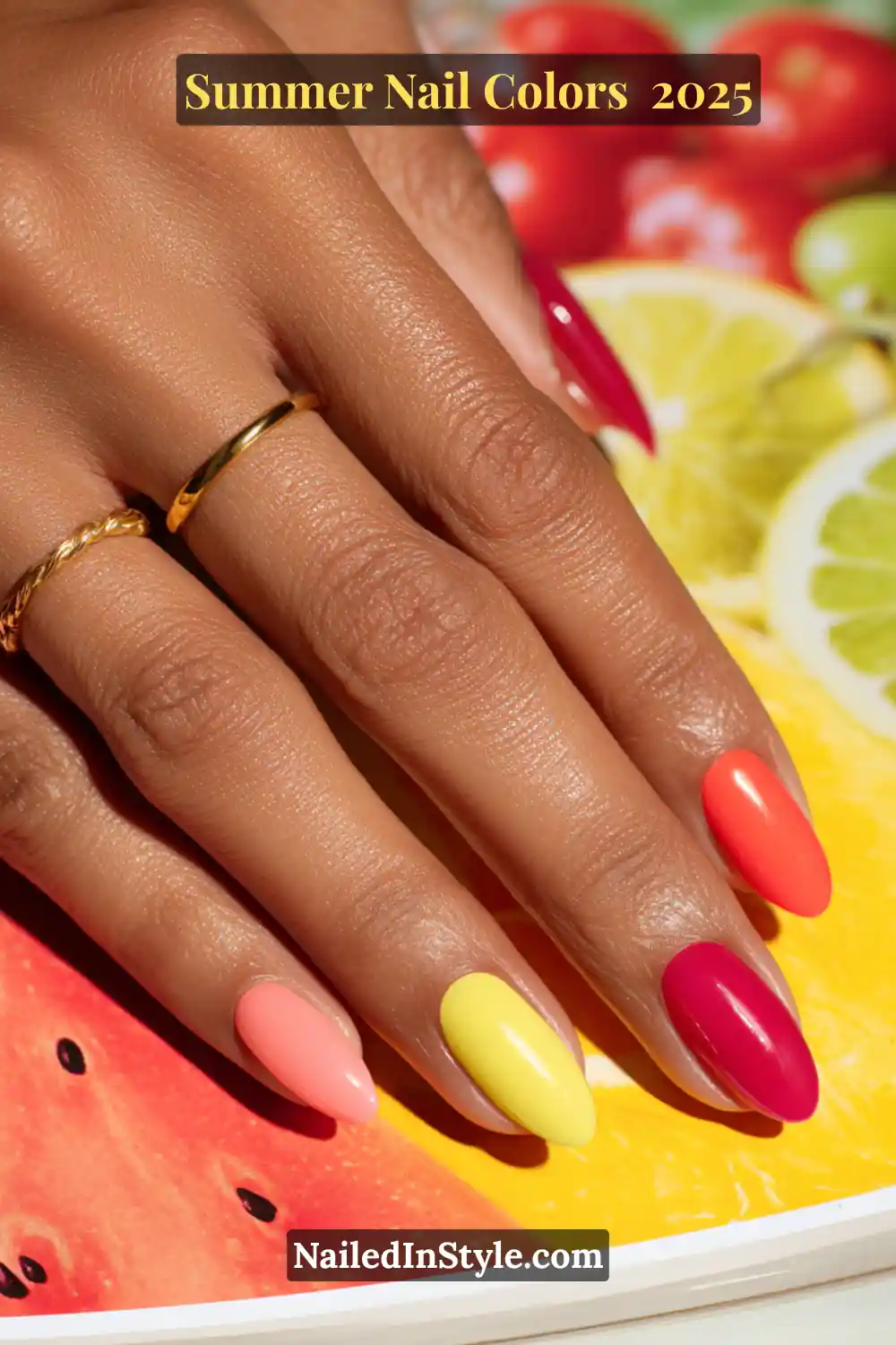 Hottest Summer Nail Colors 2026: Bold, Breezy & On-Trend 5 Hand with almond-shaped nails in bright watermelon red, lemon yellow, coral, pink, and berry tones, photographed over citrus fruits.