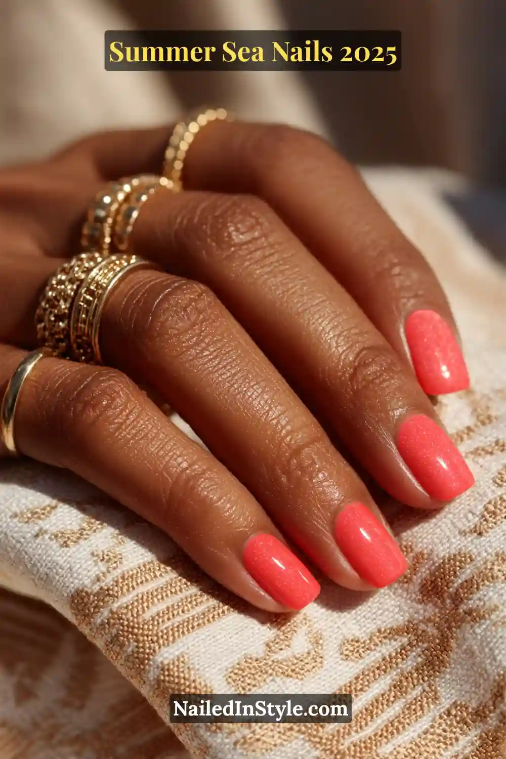 Glossy coral-pink squoval summer nails with subtle sparkle on dark skin, styled with gold rings