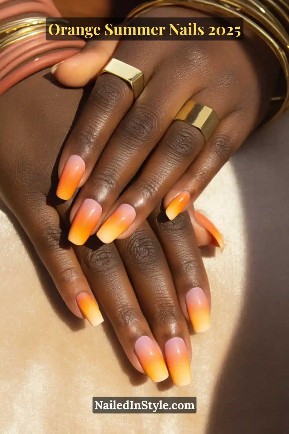 Close-up of hands with glossy orange ombré nails blending from soft pink at the base to vibrant orange tips, worn with gold jewelry.