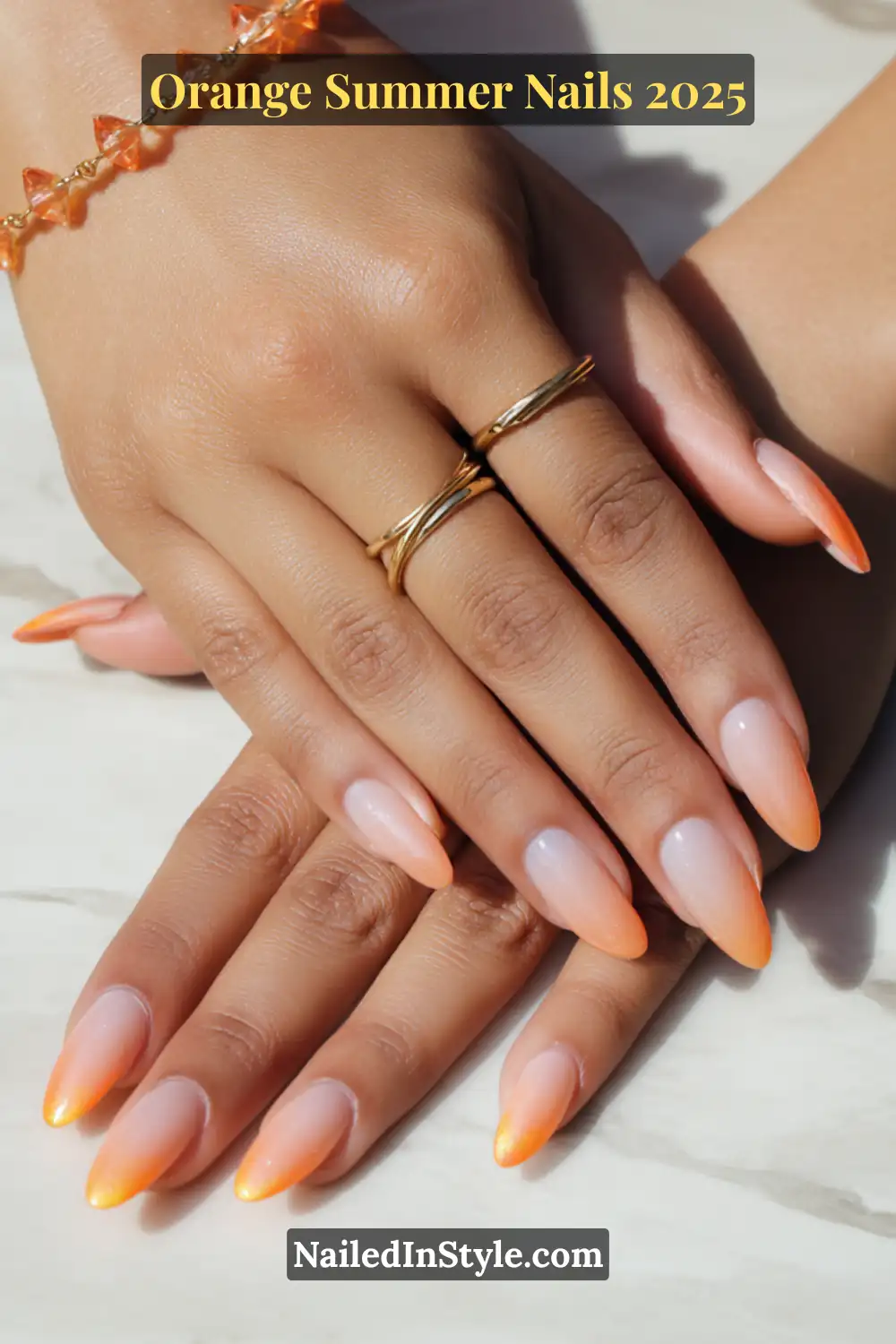 Close-up of almond-shaped nails with a soft tangerine gel fade, paired with delicate gold rings and natural lighting on a marble background.