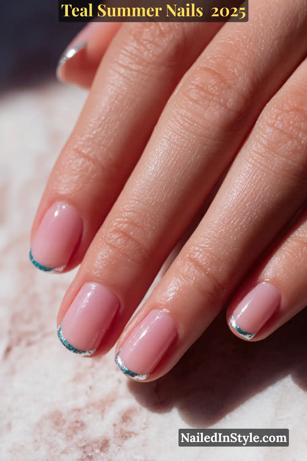 Close-up photo of a natural hand with short square nails in glossy nude polish, finished with thin teal and silver French tips, laid on a light marble surface