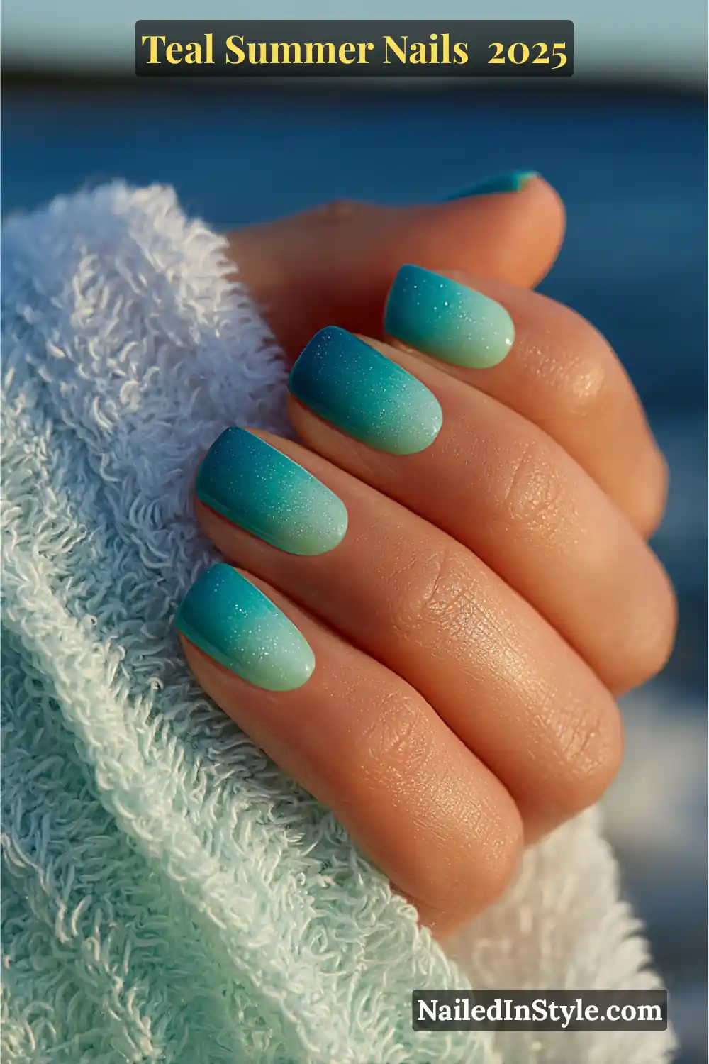 Short rounded nails with a teal-to-mint gradient and subtle shimmer, resting on a seafoam towel near the ocean