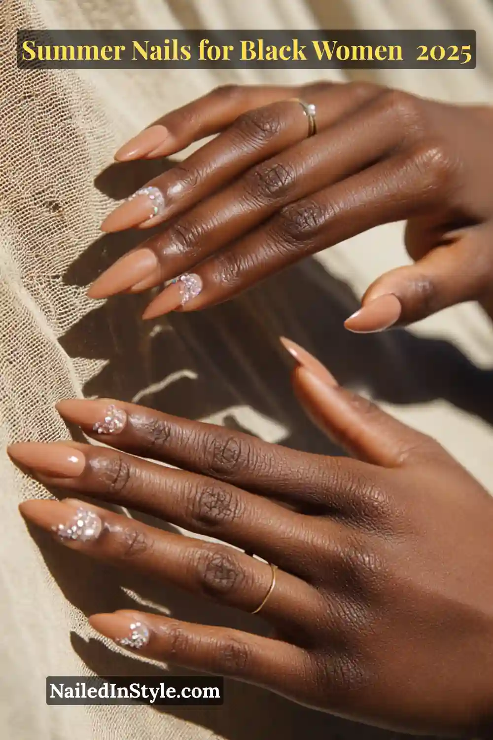 Close-up of Black woman’s hands with toffee nude almond nails and rhinestone accents, 2025 summer nail trend