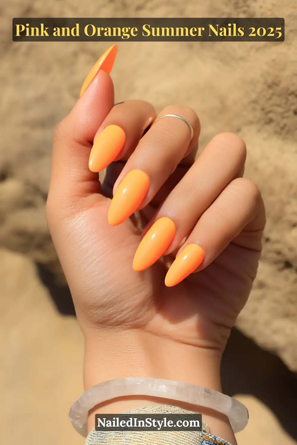 Pink and Orange Summer Nails 2026: Sunset Tips, Endless Vibes 22 Hand with almond-shaped nails painted in bright, UV-reactive tangerine polish, glowing under sunlight with a sandy background.