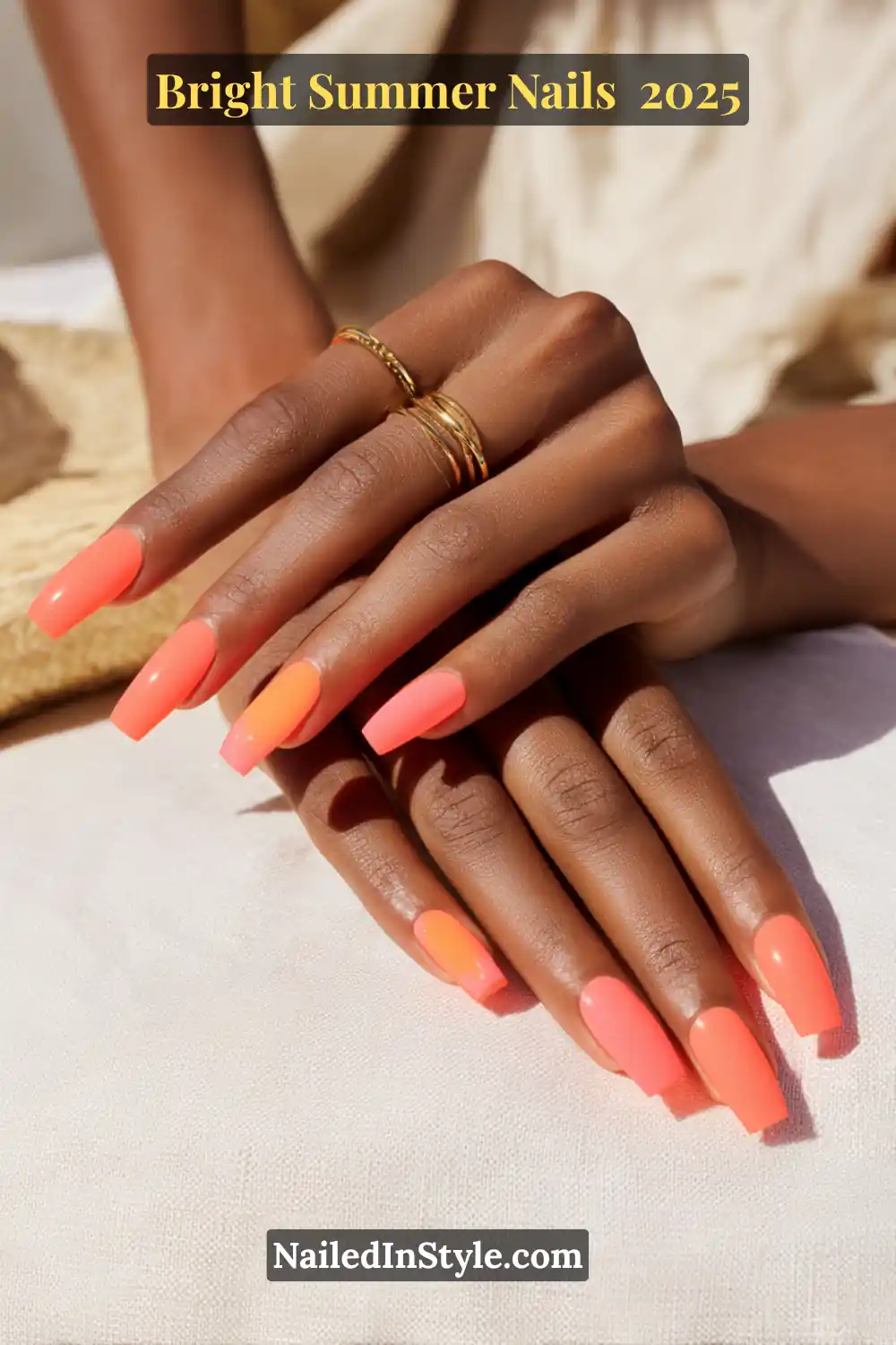 Close-up of hands with long coffin-shaped nails in vibrant coral shades, styled for summer with a minimalist gold ring.