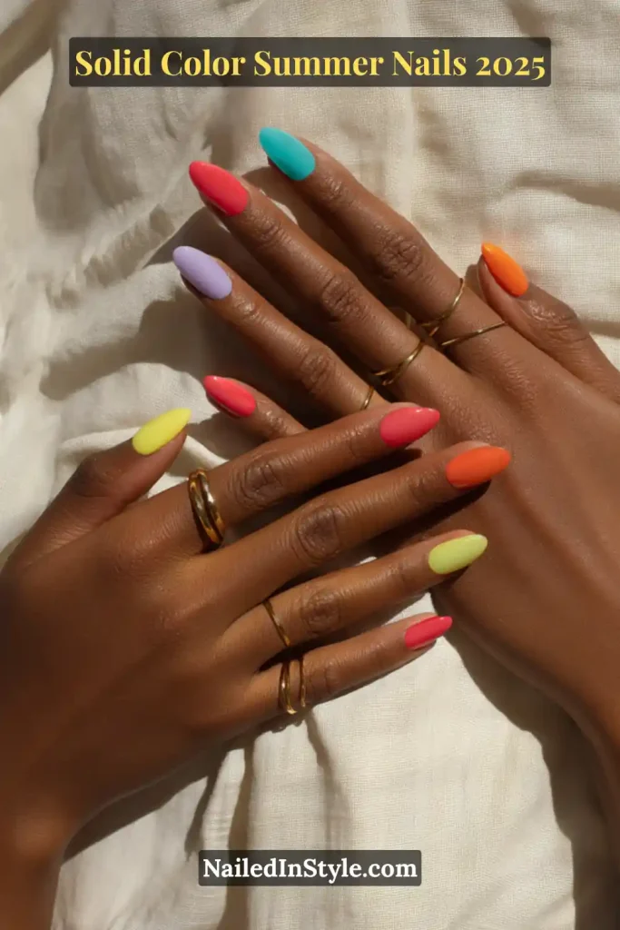 Solid Color Summer Nails Two hands with almond-shaped nails painted in solid summer shades including lavender, coral, orange, yellow, mint, and neon pink, shown against a soft white fabric background.