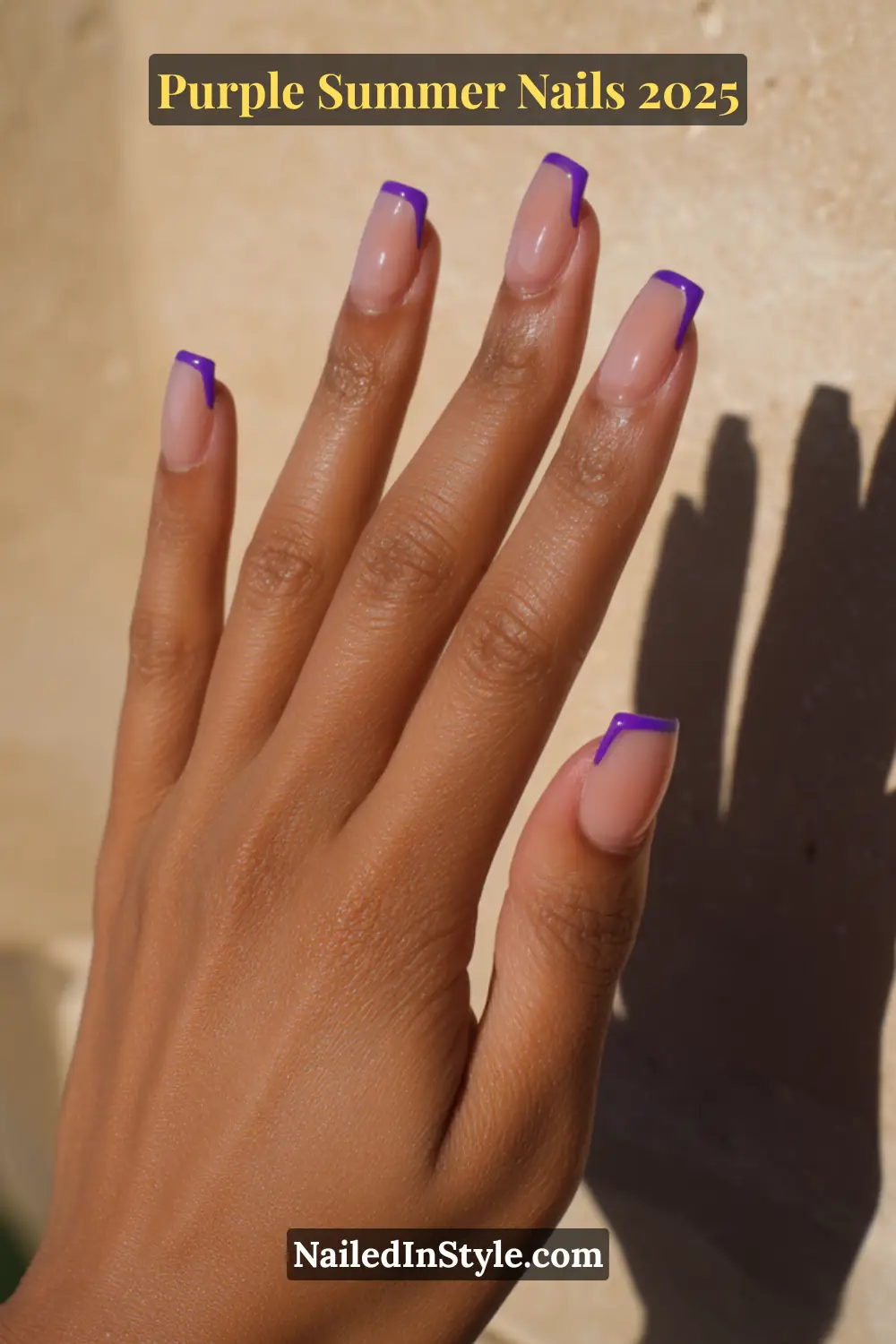 Hand with square-shaped nails featuring bold violet French tips on a nude base.