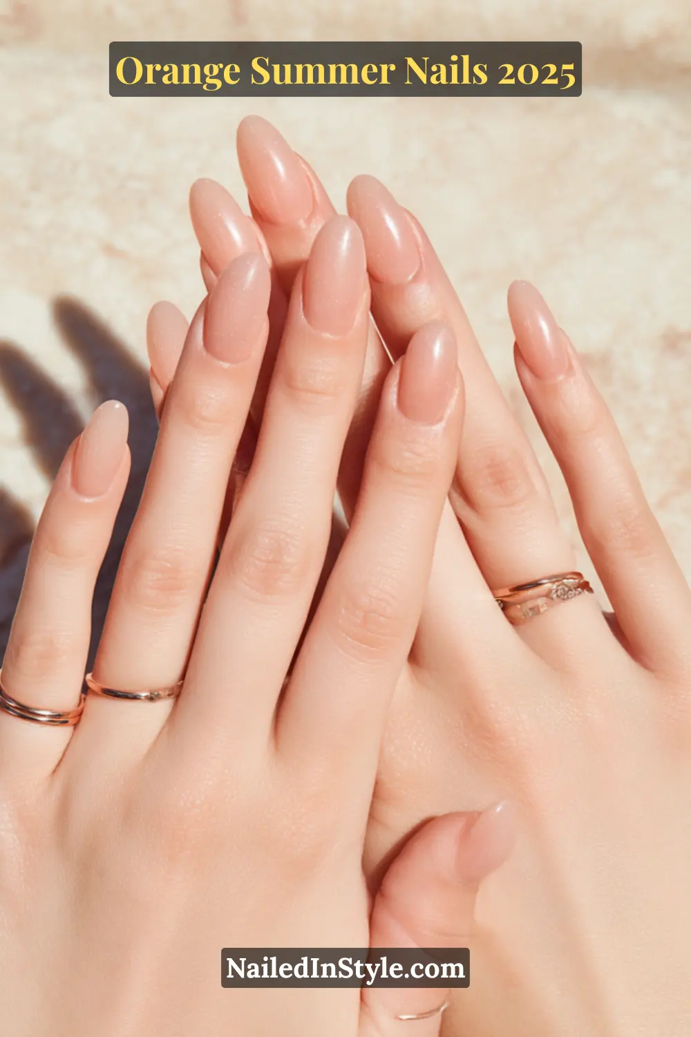 Close-up of hands with soft peach BIAB (Builder in a Bottle) nails shaped in an elegant almond style, complemented by delicate rose gold rings on a light skin tone.