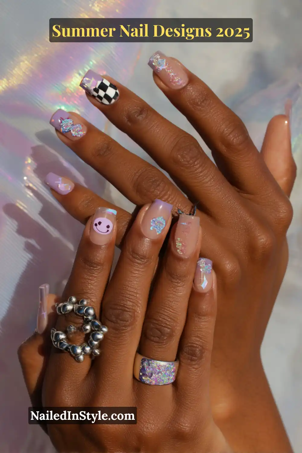 Hands with pastel nails featuring smiley faces, butterfly decals, checkerboard pattern, and sparkly overlays