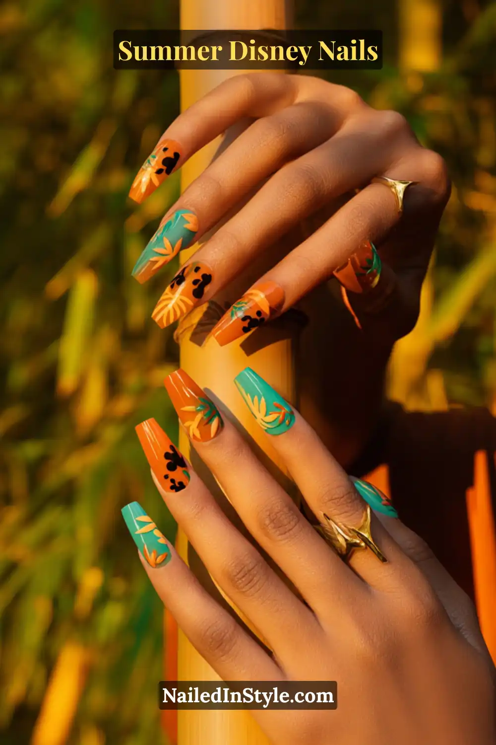 Long coffin-shaped nails in sunset orange and teal with yellow jungle leaves and black Mickey silhouettes.