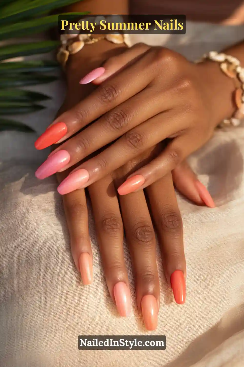Hands with almond-shaped nails featuring a shimmer ombré gradient in coral, peach, and seashell pink, styled with seashell bracelets on sunlit fabric.