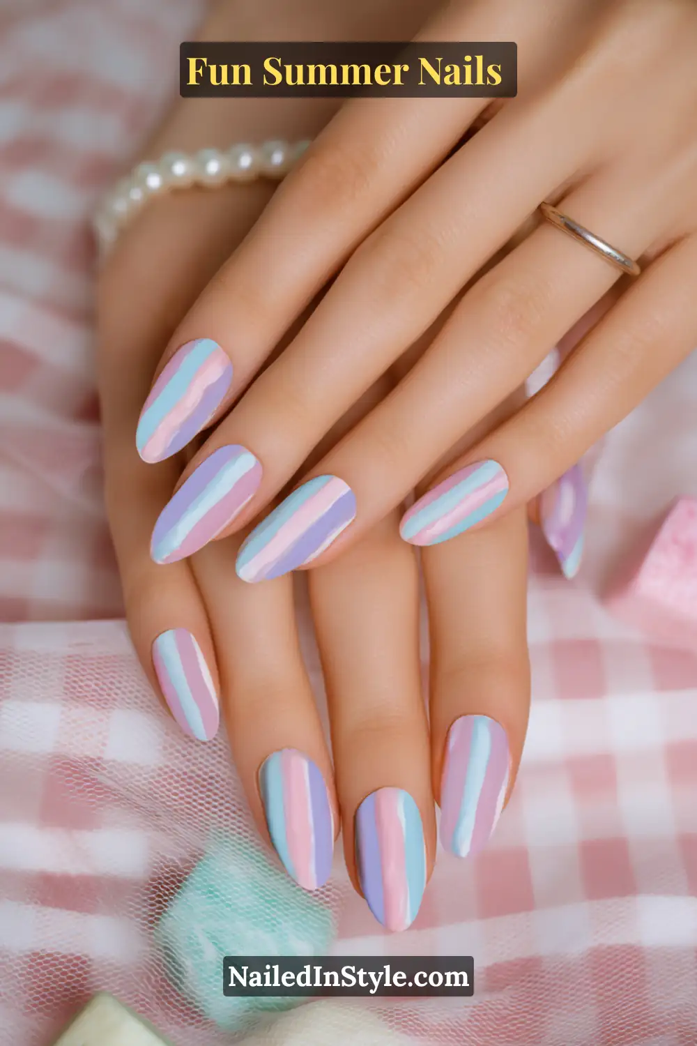 Hands with pastel striped summer nails featuring alternating shades of pink, lavender, and baby blue.