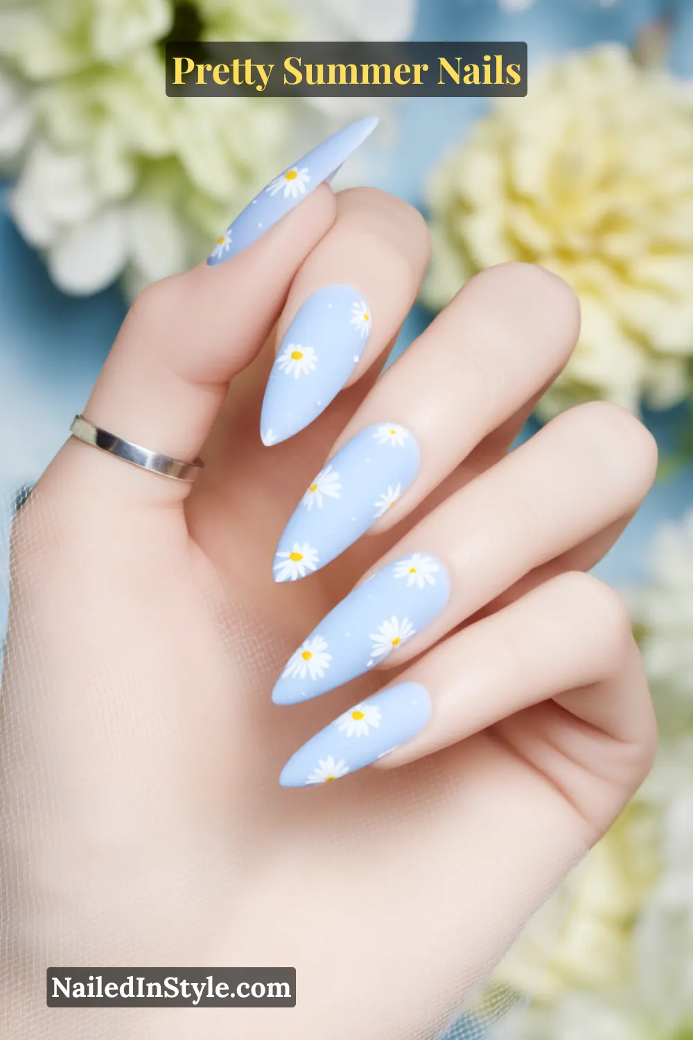 Close-up of long almond-shaped nails painted baby blue with white daisy flower designs.