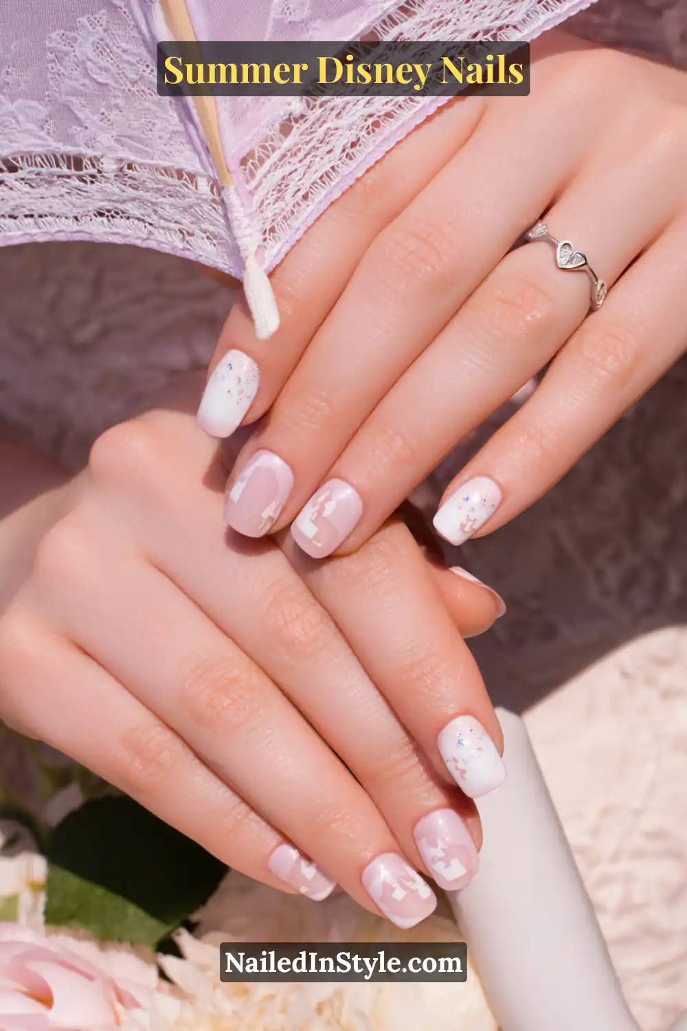 Short square nails in baby pink and white with delicate Disney character silhouettes and subtle glitter accents.
