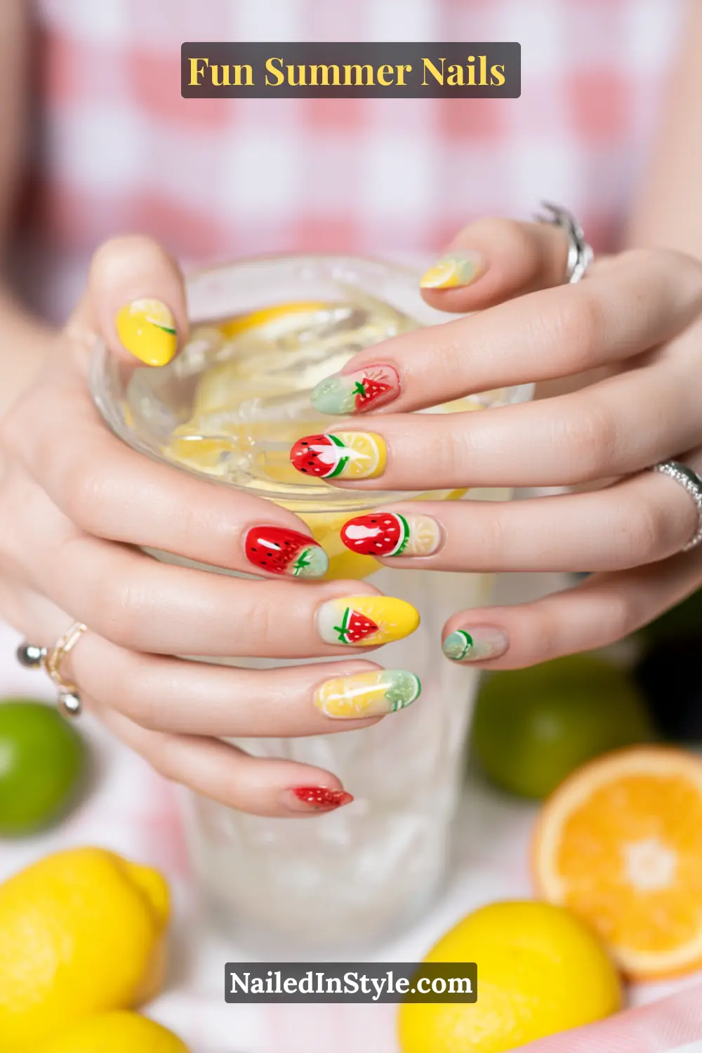 Hands with fun summer nails featuring fruity nail art designs of watermelon, lemon, and strawberry patterns.