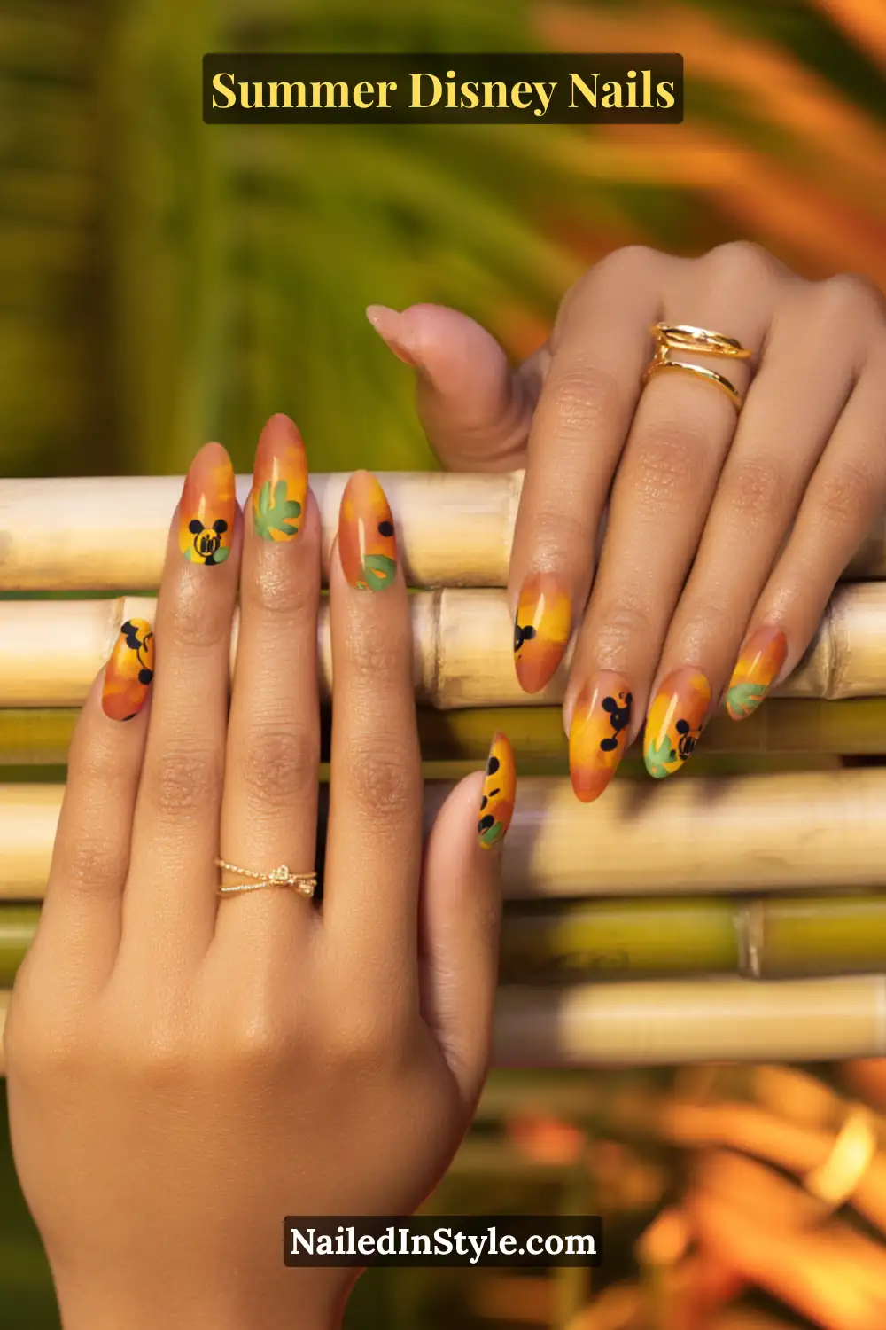 Almond-shaped nails with sunset ombre base, green tropical leaves, and black Mickey silhouettes.