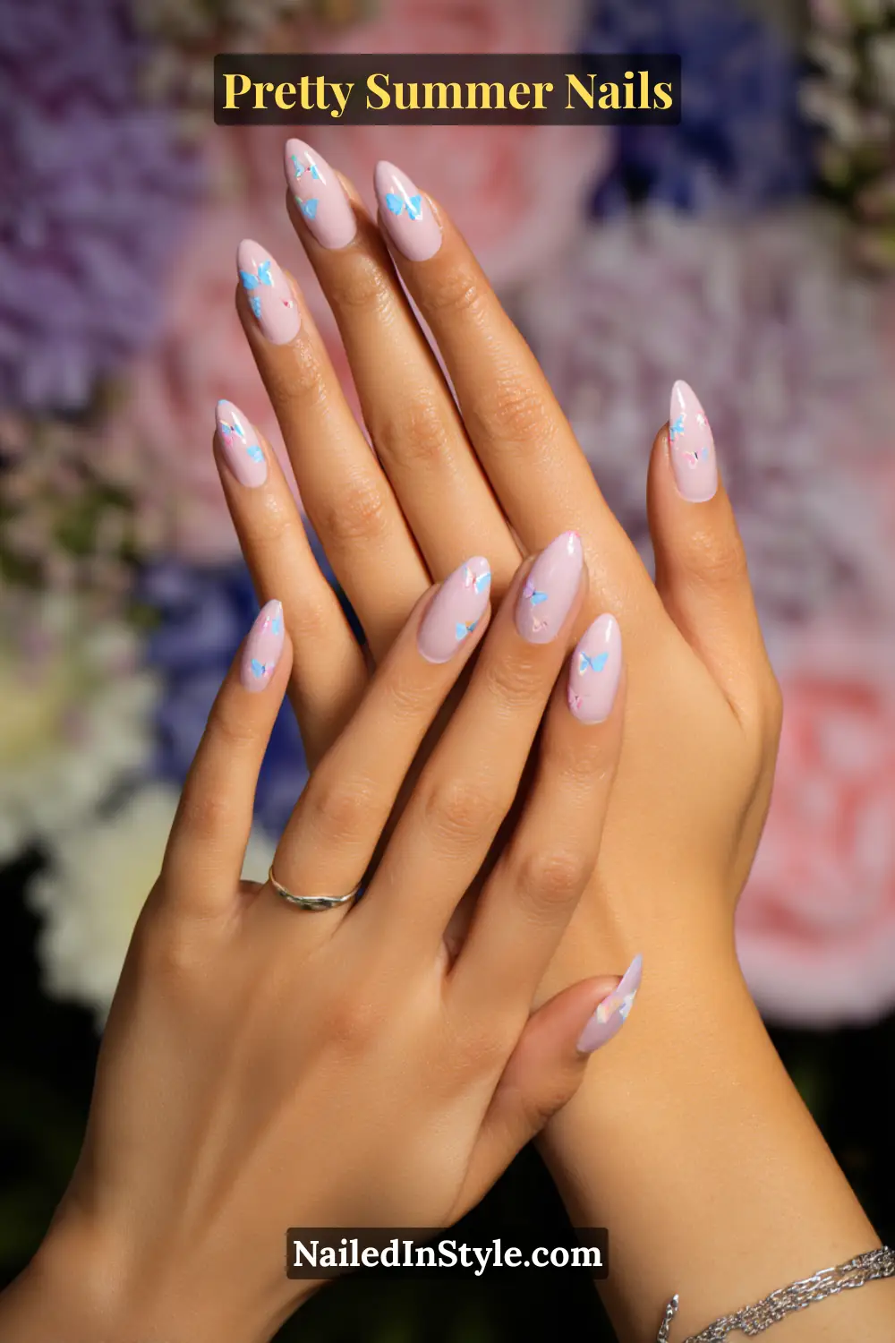 Hands with almond-shaped nude-pink nails decorated with tiny blue butterfly decals.