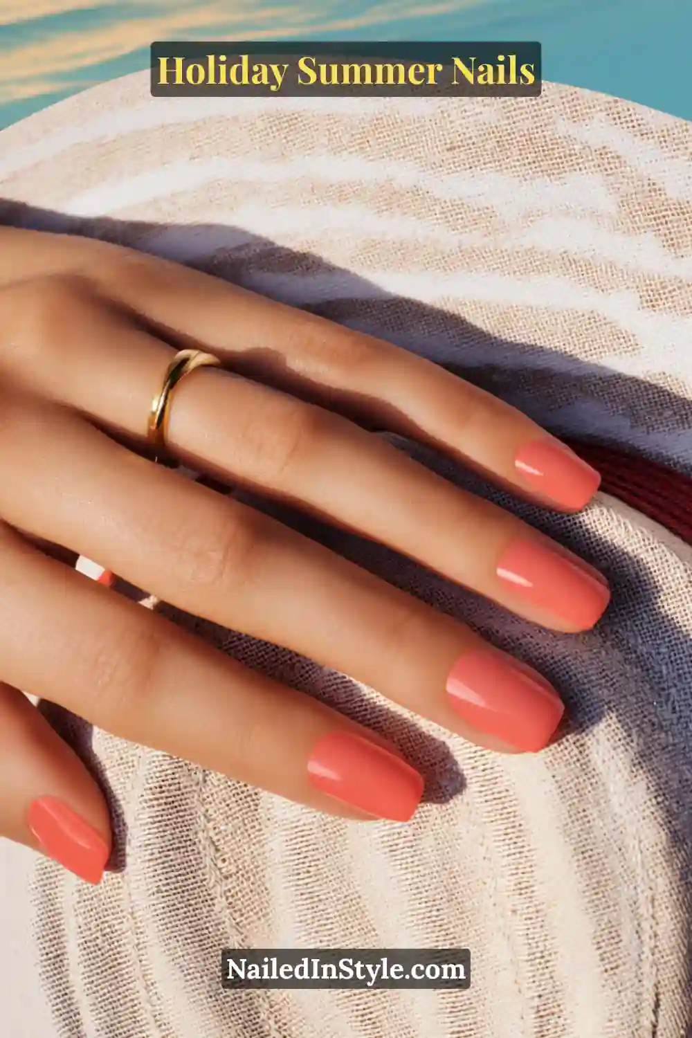 Close-up of light skin tone hand with coral holiday summer nails, paired with a soft beach background and golden ring for a chic summer vibe.